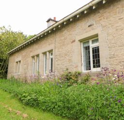 A stone exterior wall of a house with multiple windows and a flower bed with green plants and purple flowers in front at The Coach House in Shepherd's Dene near Corbridge
