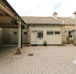 A cobblestone courtyard with potted plants around doorways and a covered parking area at The Coach House in Shepherd's Dene near Corbridge