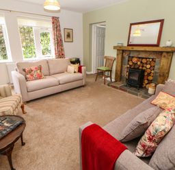 A living room with two sofas a striped armchair a wooden coffee table and a fireplace at The Coach House in Shepherd's Dene near Corbridge