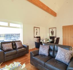 A living room with leather sofas and a dining table by a window overlooking boats at Harbourside Haven Penthouse 1 in Weymouth