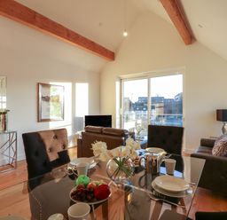 A dining and living area with glass table chairs sofas and a large window at Harbourside Haven Penthouse 1 in Weymouth