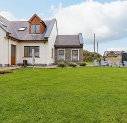 A house with a lawn a row of chairs and a shed at Cherry Blossom Cottage in Quilty County Clare