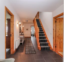 A hallway with stairs covered with a runner and a console table along the wall at Cherry Blossom Cottage in Quilty County Clare