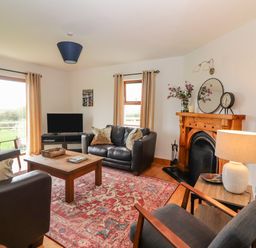 A living room with leather sofas wooden coffee table patterned rug fireplace and television at Cherry Blossom Cottage in Quilty County Clare