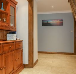 A hallway with wooden cabinetry on the left a photo on the wall and a wooden staircase on the right at Meadowside in Goonhavern