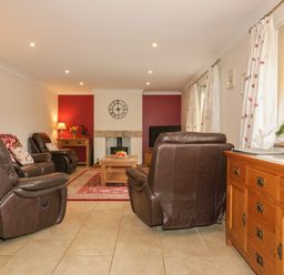 A living room with brown leather armchairs a wooden coffee table a red patterned rug and a wooden cabinet by a window at Meadowside in Goonhavern