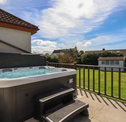 An outdoor patio with a hot tub and steps overlooking a grassy yard and a small white shed at Meadowside in Goonhavern