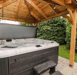 An outdoor hot tub with bubbling water under a wooden pavilion surrounded by greenery at Reybridge House in Lacock