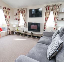 A living room with a grey sofa patterned curtains and a wall-mounted television at Two Little Ducks in Cayton