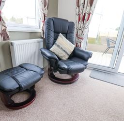 A black leather armchair with a cushion and matching footstool near a window and glass door at Two Little Ducks in Cayton