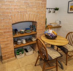 A small dining area with a round wooden table and two wooden chairs with cushions next to shelves inside a brick alcove with dishes and glassware at The Escape in Malvern