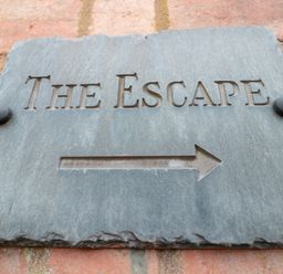 A directional stone sign with the words The Escape and an arrow on a brick wall at The Escape in Malvern