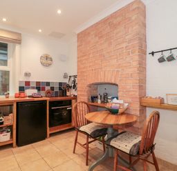 A kitchen with a wooden table and two chairs next to a brick fireplace and a counter with a sink oven and fridge at The Escape in Malvern