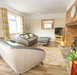 A living room with grey sofas yellow plaid curtains a brick fireplace and a television at Dove's Nest in Martham