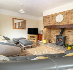 A living room with a brick fireplace a clock on the mantel a television a sofa ottomans and a rug at Dove's Nest in Martham