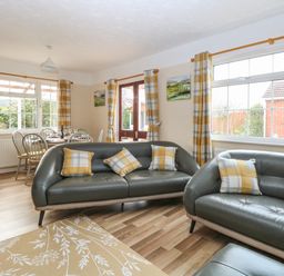 A living room with two gray sofas with plaid cushions and a dining table with chairs near windows at Doves Nest in Martham