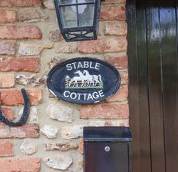 A brick wall with a horseshoe a lamp a plaque reading Stable Cottage and a black mailbox next to a dark wooden door at Stable Cottage in Colyton