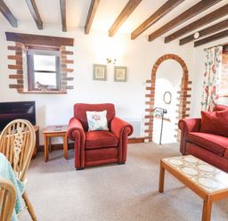 A living room with red armchair and sofa wooden beams on ceiling and arched brick doorway at Stable Cottage in Colyton