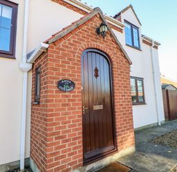 The front entrance of a house with a small brick porch and a wooden arched door at Anvil Cottage in Appleton Wiske