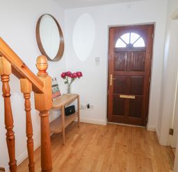 An entrance hallway with a wooden staircase a wooden table with flowers a round wall mirror and a wooden front door at 1 Closheen Lane Rosscarbery County Cork