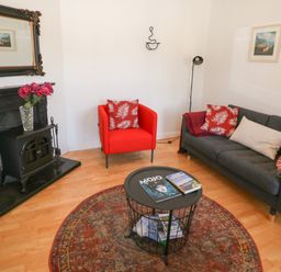 A living room with a gray sofa and red chair with patterned cushions a round coffee table and a fireplace at 1 Closheen Lane Rosscarbery County Cork