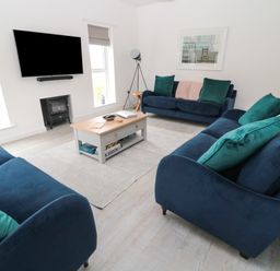 A living room with three blue sofas, a coffee table, a TV mounted on the wall, and a small stove at Summer Rose in Craster
