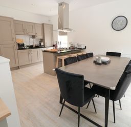 A kitchen with beige cabinets a black countertop an island with stools and a dining table with black chairs at Summer Rose in Craster