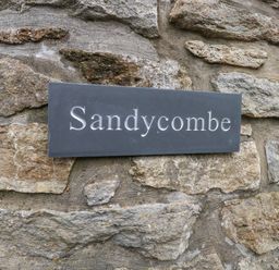 A sign reading Sandycombe mounted on a stone wall at Sandy Combe in West Bay