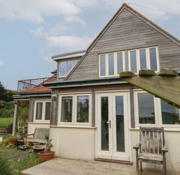 Exterior view of a two-story house with wooden and cream walls and garden furniture at Sandy Combe in West Bay