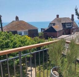 A view from a balcony with a railing overlooking houses trees and the sea at Sandy Combe in West Bay