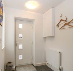 An entryway with a white door that has four small windows wooden coat hangers on hooks a radiator and a ceramic jug on the floor at Hen Gapel in Waunfawr Gwynedd