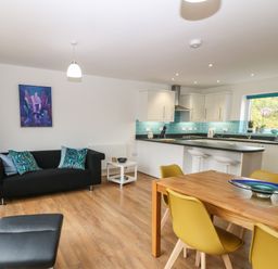 An open plan living room and kitchen with black sofa wooden dining table and yellow chairs at Hen Gapel in Waunfawr Gwynedd