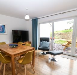 A dining area with a wooden table and yellow chairs next to a black chair and ottoman by sliding glass doors at Hen Gapel in Waunfawr Gwynedd