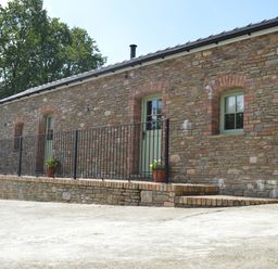 An exterior view of a stone building with green doors and windows a black metal railing and potted plants on the ledge at Cwrt y Wennol in Salem near Clydach