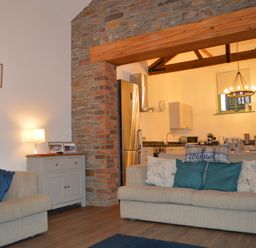 A living room with beige sofas and cushions next to a small cabinet with a lamp and photos at Cwrt y Wennol in Salem near Clydach