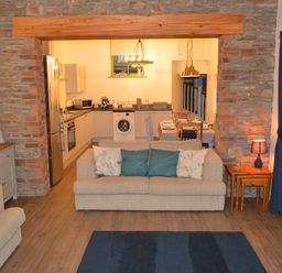 A living room with beige sofas and blue cushions next to a kitchen with white cabinets and dining table at Cwrt y Wennol Salem near Clydach