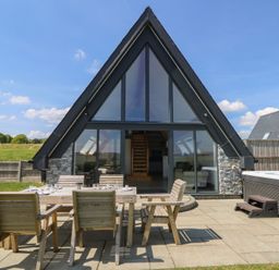 An outdoor patio with wooden table and chairs and a hot tub outside an a frame house at Hill Radnor - The Sheepfold in Llanyre near Llandrindod Wells