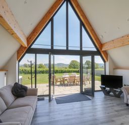 A living room with sofas a TV on a stand a coat rack and large glass doors opening to a patio with outdoor furniture at Hill Radnor - The Sheepfold in Llanyre near Llandrindod Wells