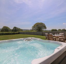 An outdoor area with a hot tub and a dining table with chairs on a patio at Brecknock Cheviot - The Sheepfold in Llanyre near Llandrindod Wells