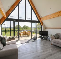 A living room with two sofas a television and large glass doors opening to an outdoor dining area at Brecknock Cheviot - The Sheepfold in Llanyre near Llandrindod Wells