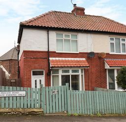 A two-story house with a red tiled roof and a green wooden fence with a private road sign at Over Esk in Whitby