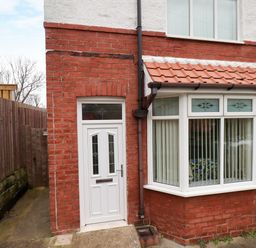 An exterior view of a brick house with a white door and bay window with vertical blinds at Over Esk in Whitby