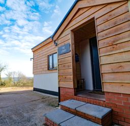 The entrance of a wooden house with steps leading to a door and a landscape in the background at The Linhay in Cadeleigh near Tiverton
