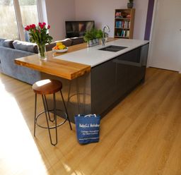 A kitchen island with a sink wooden bar stool and flowers next to a living room with a sofa and television at The Linhay Cadeleigh near Tiverton
