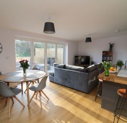 A living room with a gray sofa a round wooden dining table with chairs and a kitchen counter with bar stools at The Linhay in Cadeleigh near Tiverton