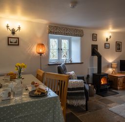 A dining table set for breakfast next to an armchair and wood-burning stove in a living room at Wavering in Compton Bishop near Axbridge