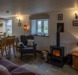 A living room with a wood burning stove an armchair a dining table and open wooden door at Wavering in Compton Bishop near Axbridge