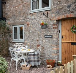 A stone house exterior with wooden door and small garden table with chairs at Wavering Compton Bishop near Axbridge