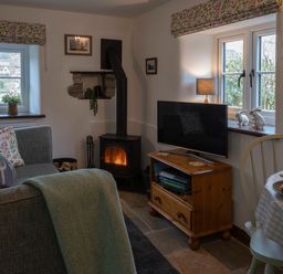 A living room with a sofa a wood burning stove a television on a wooden stand and a dining table at Crooks in Axbridge