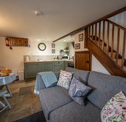 A small kitchen and dining area with green cabinets a gray sofa and wooden stairs at Crooks in Axbridge